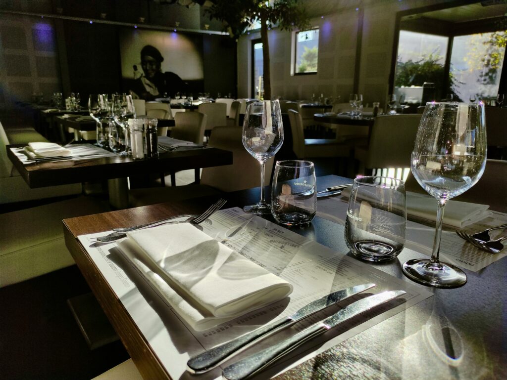 Sunlit restaurant table setting with wineglasses and cutlery, creating a warm dining atmosphere.