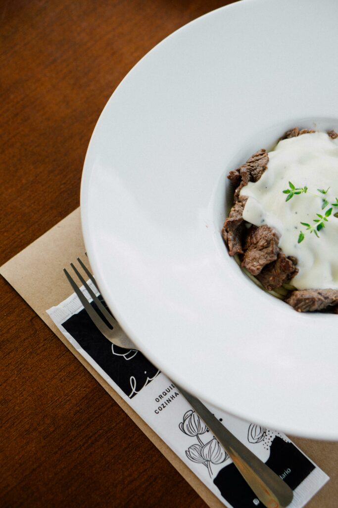 Close-up of a gourmet dish with meat and sauce, garnished with thyme, served on a white plate.