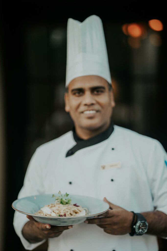 Professional chef in uniform proudly presenting a delicious pasta dish indoors.
