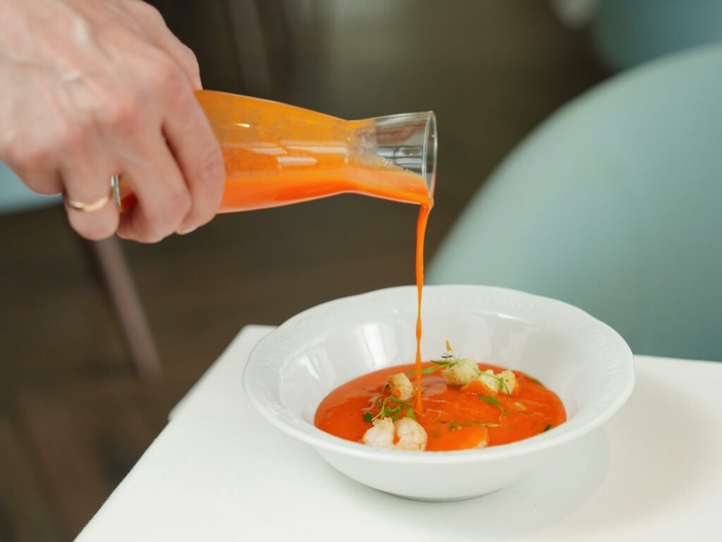 Hand pouring red sauce over a finely plated seafood dish in a restaurant setting, adding flavor and visual appeal.