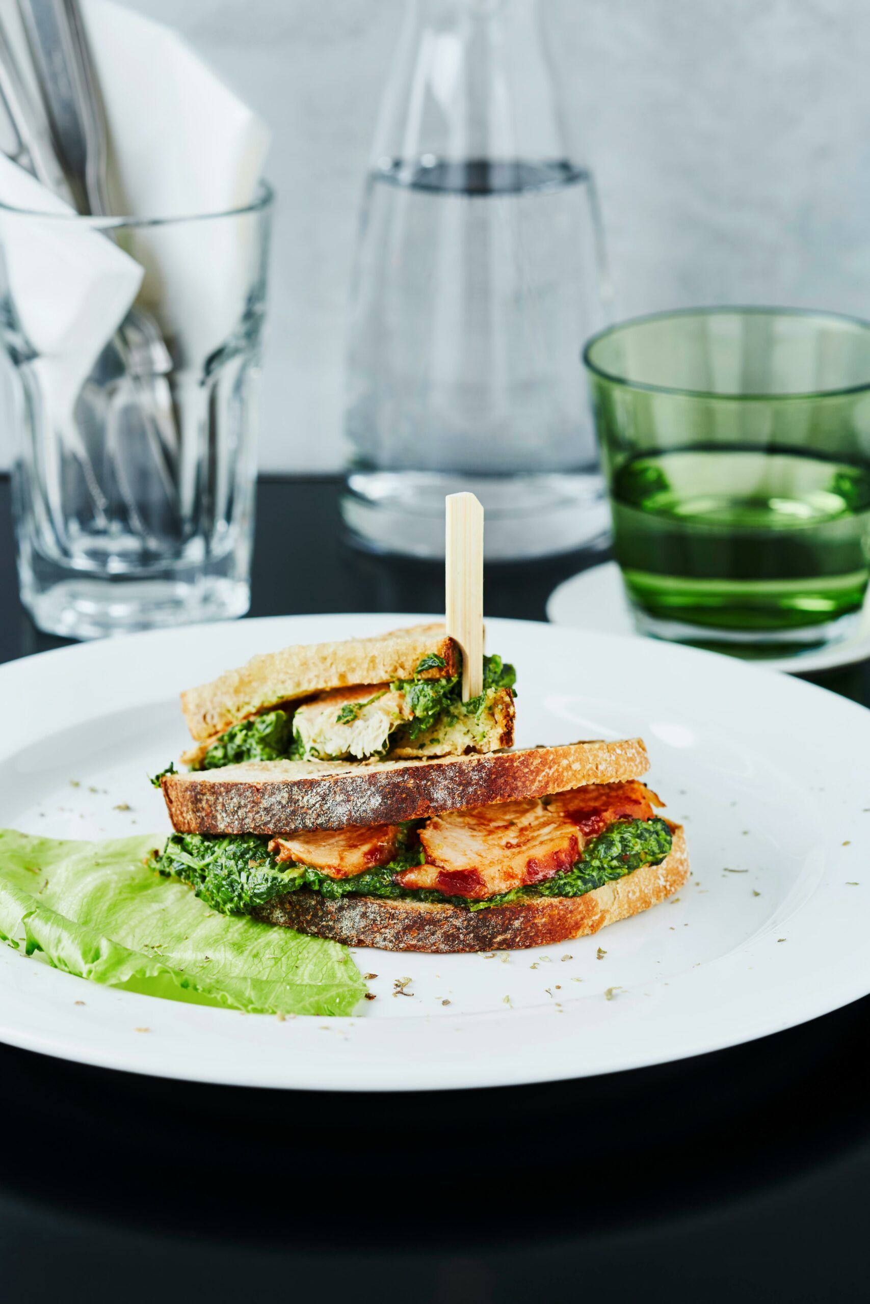 Delicious grilled chicken sandwich with spinach on a white plate served indoors.